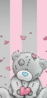 Gray teddy bear holds pink heart on striped background.