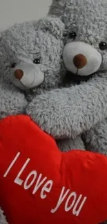 Two grey teddy bears hug a red heart pillow with 'I Love You' text.