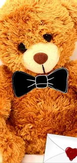 Cute teddy bear with a black bow tie and red heart envelope.