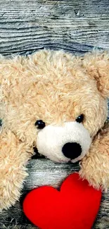 Cute teddy bear with a red heart on wood background.