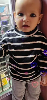 Adorable toddler in striped sweater by a sunny window.