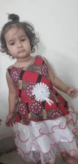 Adorable toddler in a floral dress standing indoors.