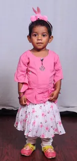 Cute toddler in pink outfit with floral skirt on wooden floor.