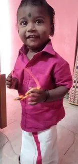 Adorable toddler in pink outfit smiling indoors.