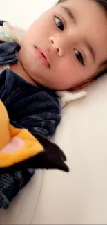 Adorable toddler with a plush toy lying on a soft surface.