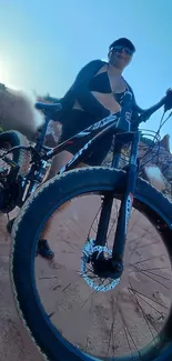 Cyclist on mountain trail with blue sky background.