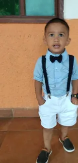 Child in blue shirt, white shorts, with orange wall.