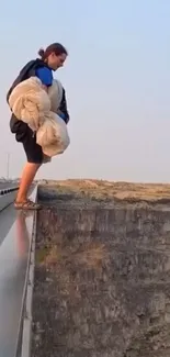 Person daringly stands on cliff edge at sunset.