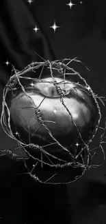 Dark metallic apple wrapped in barbed wire on black background.