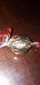 Dark chocolate candy elegantly wrapped in red foil on dark wood.