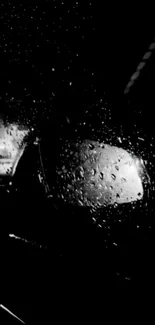 Raindrops on glass, dark night view with reflection in black and white.