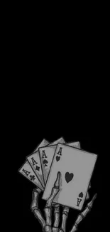 Skeleton hand holding playing cards on dark background.