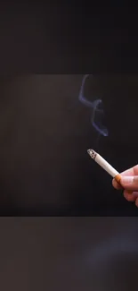 Hand holding a lit cigarette with smoke against a dark brown background.