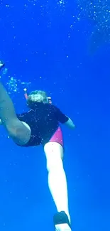 Person diving in deep blue ocean with vibrant underwater scenery.