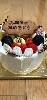 Birthday cake with fruit toppings and a message on a wooden floor.