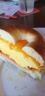Scrambled eggs and cheddar cheese bagel sandwich on a white plate.