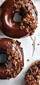 Three chocolate donuts with crunchy toppings on a textured surface.