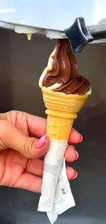 Hand holding chocolate soft serve ice cream cone.