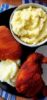 Crispy fried chicken served with mashed potatoes on a black plate.