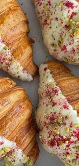 Four glazed croissants with pistachio topping on a tray.