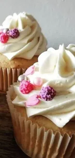 Two cupcakes with cream frosting and colorful sprinkles on a wooden surface.