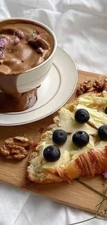 A cup of coffee with a blueberry pastry on a wooden board.