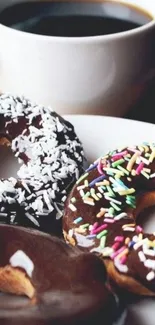 Close-up of three donuts with sprinkles and a cup of coffee.