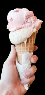 Hand holding a two-scoop ice cream cone against a white background.