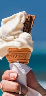 Hand holding ice cream cone with blue sky background.