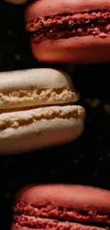 Close-up of pink and cream macarons on a dark background.