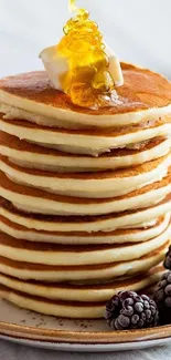 Tall stack of pancakes with syrup and berries.