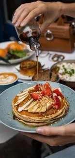 Stacked pancakes with syrup, strawberries, and banana slices on a blue plate.