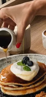 Pancakes topped with syrup and blueberries on a wooden table.