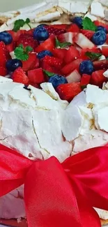 Beautiful pavlova with fresh berries and a red ribbon decoration.