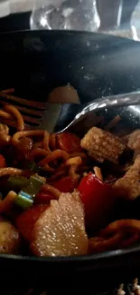 Colorful stir-fry noodles in black bowl with vegetables.