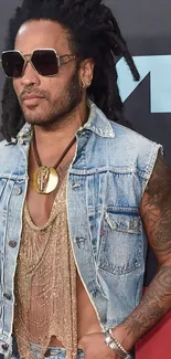 Person in denim vest and sunglasses with tattoos at VMA event.