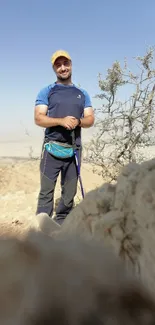 Man standing in desert landscape, with clear blue sky and rocky terrain.