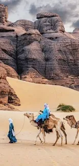 Camels in a majestic desert landscape with sand dunes and rocky cliffs.