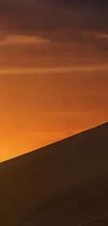 Desert sunset with dune silhouette and orange sky.