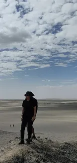 Person standing on a desert hill with cloudy sky in the background.