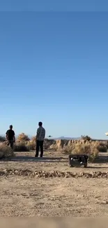 Two people in a vast desert under a clear blue sky.