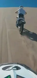 Motorcyclists ride up sandy dunes in the desert under a blue sky.