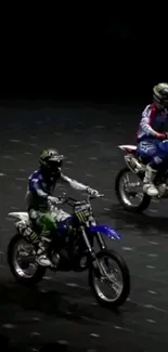 Two motorbike riders performing stunts on a track under bright lights.