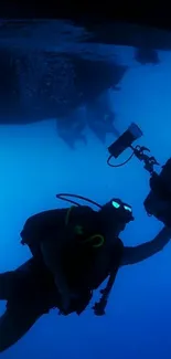 Diver capturing underwater scenery with camera against deep blue backdrop.