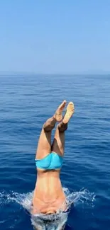 Diver making a splash into the blue ocean waters with clear skies above.