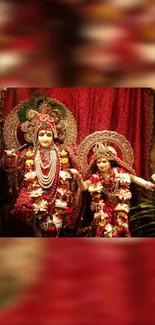 Divine Hindu deities decorated in red attire against a vibrant backdrop.