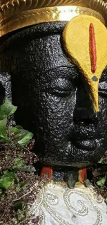 Divine stone idol with gold headdress and lush greenery.