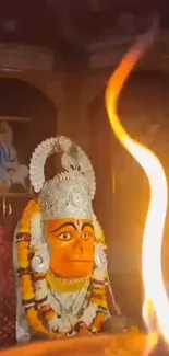 Orange Hanuman statue with temple flame in foreground, vibrant colors.