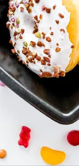 Glazed donut on a black plate with colorful candies on a white background.