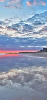 Sunset over a beach with a castle, reflecting a colorful sky in calm waters.